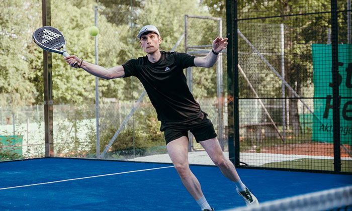 Ein Mann, der einen Ball beim Padel zurück schlägt.